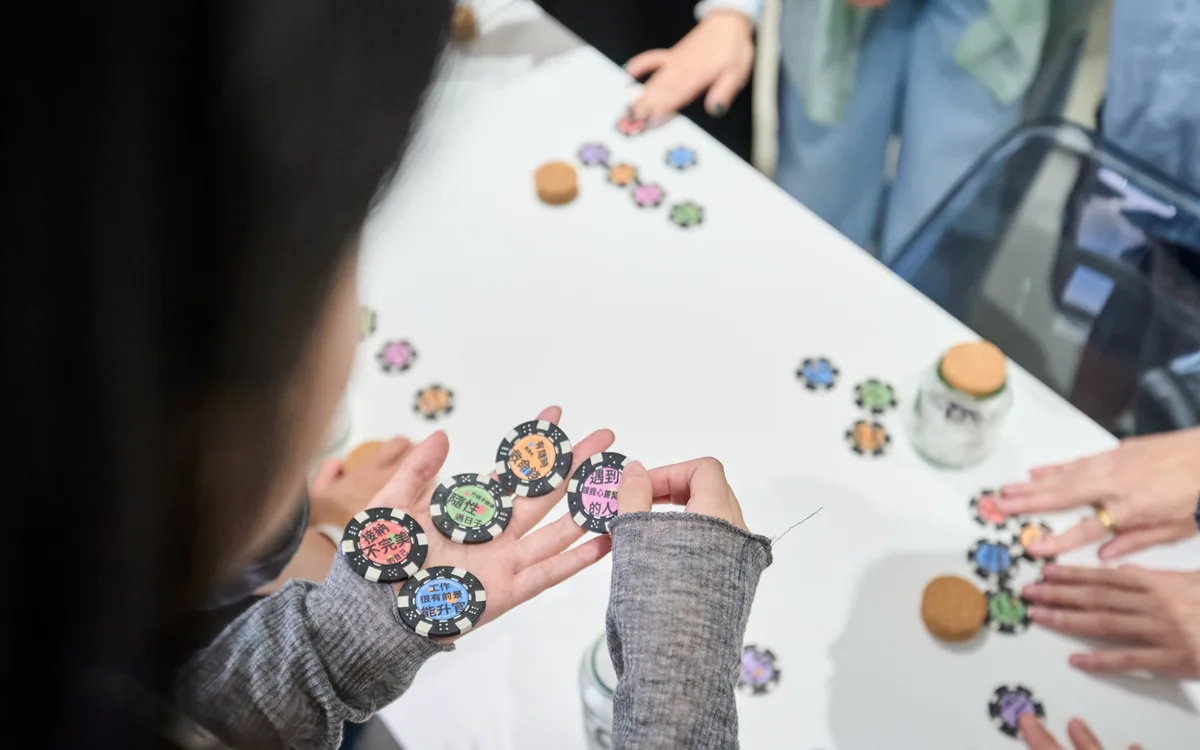 桌上散落著寫滿人生選項的彩色籌碼，有人手裡握著「接納不完美的自己」「工作很有前景能升官」等幾枚籌碼
